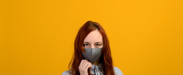 Portrait d'une jeune fille dans un masque, qui met un gant en caoutchouc. Fond jaune, studio