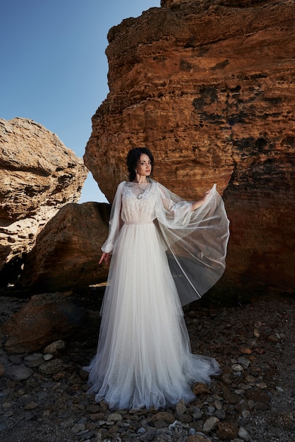 Portrait d'une jeune fille dans une robe magnifique de mariage posant un photographe sur la plage. La mariée est sur les rochers