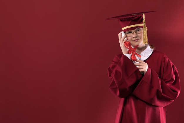 portrait d'une jeune fille diplômée dans un bonnet de graduation sur fond rouge