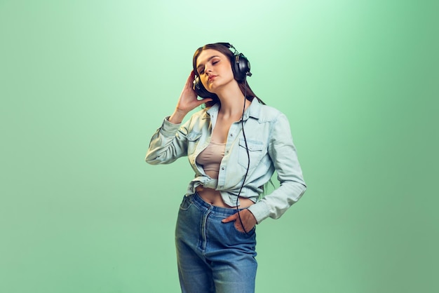 Portrait de jeune fille émotive dans des vêtements décontractés écoutant de la musique dans des écouteurs isolés sur