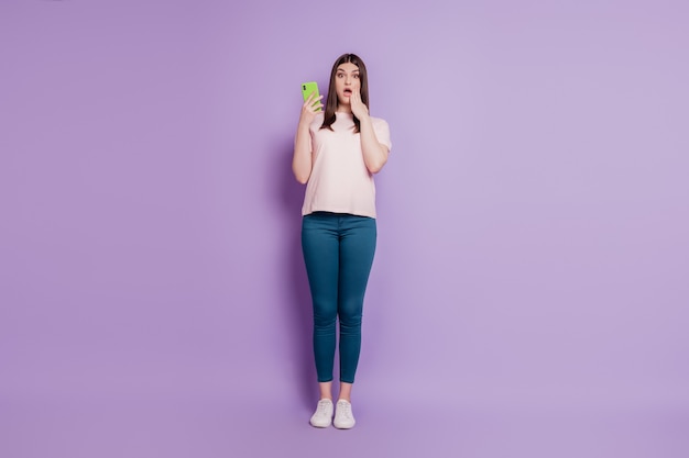 Portrait de jeune fille étonnée excitée tenir la joue de paume de téléphone portable bouche ouverte sur fond violet