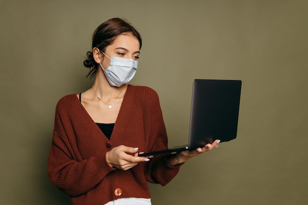 Portrait d'une jeune fille étudiante dans un masque de protection avec un ordinateur portable sur fond vert