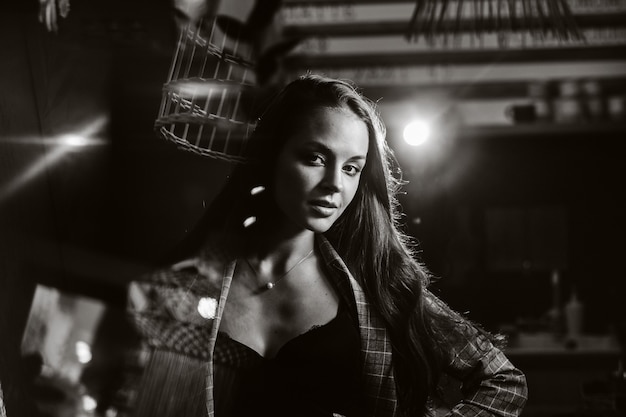 Portrait d'une jeune fille européenne aux cheveux longs dans un café dans la lumière du soir, une grande fille dans une veste aux cheveux longs dans un café. photo en noir et blanc.