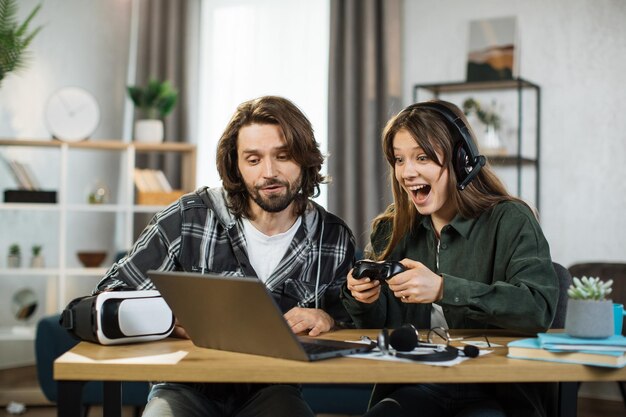 Portrait d'une jeune fille excitée et concentrée jouant dans un jeu vidéo à l'aide d'un ordinateur portable et d'un joystick