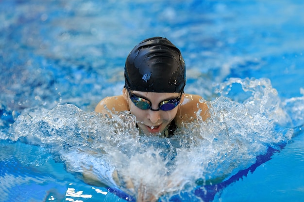 Portrait d'une jeune fille en gros plan dans des lunettes et une casquette de natation style papillon dans la piscine d'eau bleue.