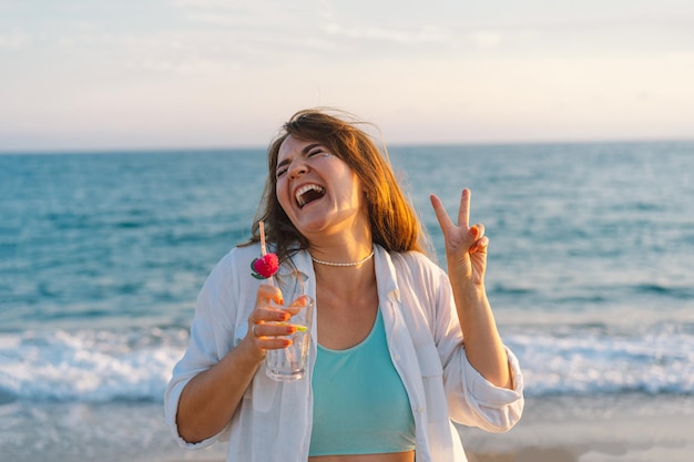 Portrait d'une jeune fille heureuse avec un cocktail à la main sur un fond de belle mer