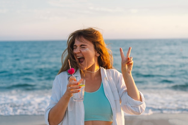 Portrait d'une jeune fille heureuse avec un cocktail à la main sur un fond de belle mer