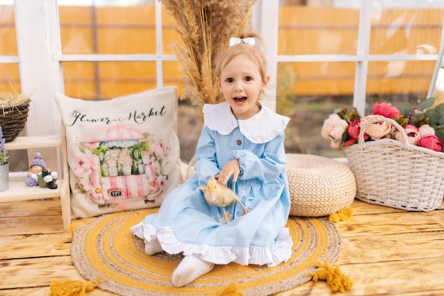 Portrait d'une jeune fille heureuse et excitée jouant avec un petit canard jaune assise sur le sol en bois d'une maison de gazebo d'été un jour ensoleillé