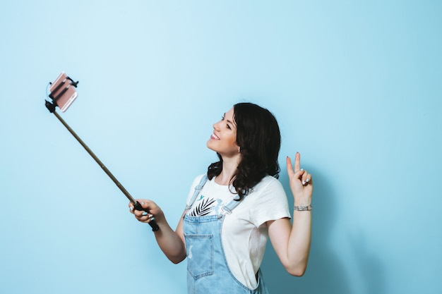 Portrait d'une jeune fille heureuse faisant selfie isolé sur mur bleu