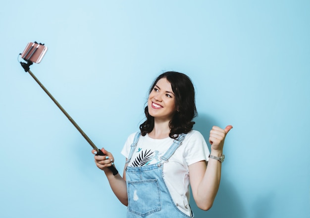 Portrait d'une jeune fille heureuse faisant selfie isolé sur mur bleu