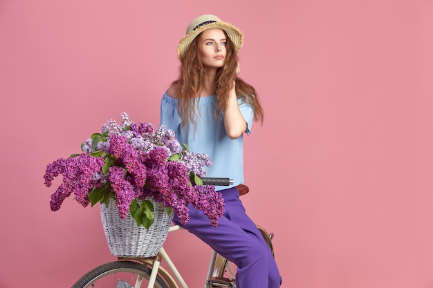 Portrait d'une jeune fille heureuse avec vélo vintage et fleurs sur fond rose.