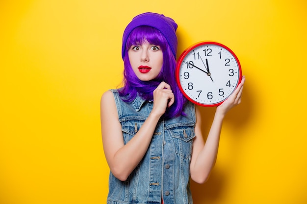 Portrait de jeune fille hipster de style aux cheveux violets avec une grande horloge sur fond jaune