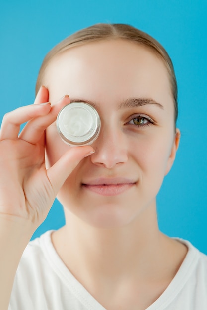 Portrait de jeune fille joyeuse couvrant ses yeux par une crème peut. Elle regarde la caméra et rit.