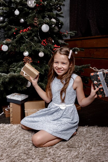 Portrait d'une jeune fille joyeuse habillée en robe tenant des coffrets cadeaux de Noël