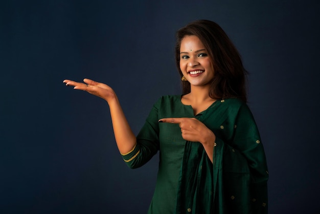 Portrait d'une jeune fille joyeuse réussie tenant et présentant quelque chose à portée de main avec un visage souriant heureux