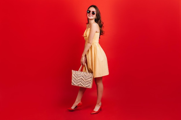 Portrait d'une jeune fille en lunettes de soleil et sac de paille sur fond rouge