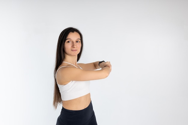 Portrait de jeune fille mature étirant ses bras sur fond blanc Jolie femme brune en vêtements de sport à la mode exerçant un concept de sport de mode de vie sain