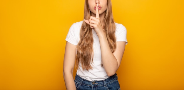 Portrait de jeune fille montrant chut signe isolé sur jaune