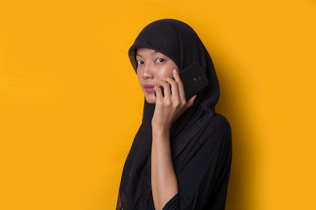 Portrait de jeune fille musulmane à l'aide d'un smartphone sur fond jaune