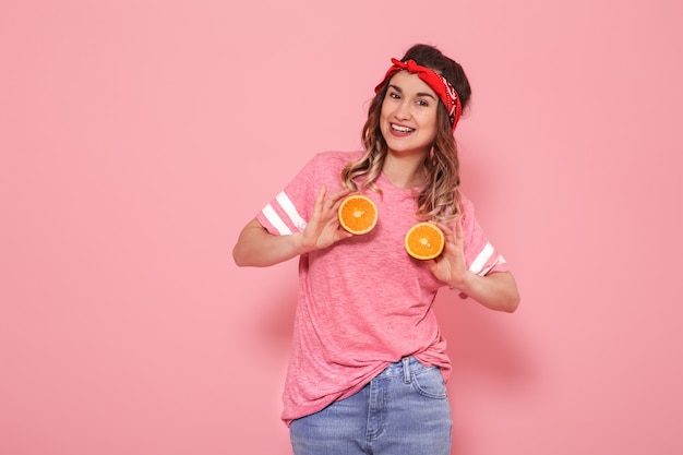 Portrait d'une jeune fille avec des oranges à la main, sur un mur rose