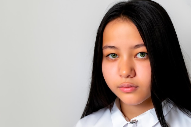 Portrait d'une jeune fille d'origine asiatique aux yeux verts, de longs cheveux noirs et une chemise à col blanc sur un fond blanc