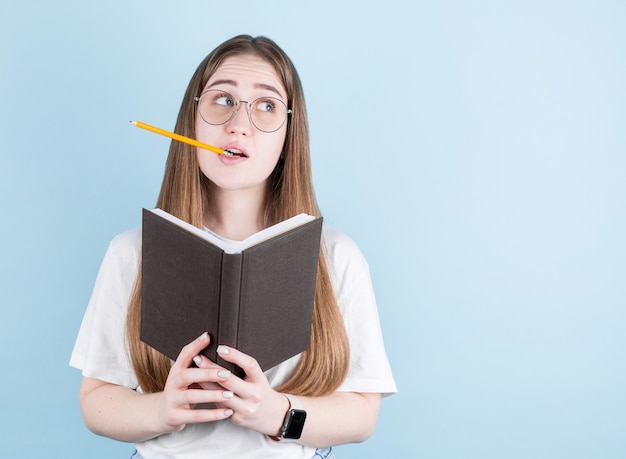 Portrait de jeune fille pensive réfléchie ayant un cahier et un crayon dans la bouche