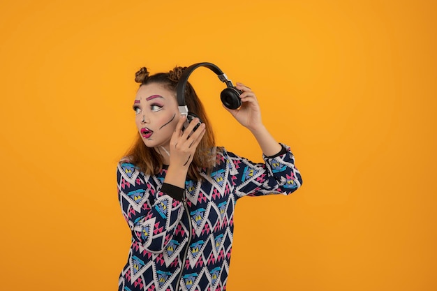 Portrait de jeune fille portant un maquillage créatif et tenant ses écouteurs tout en regardant de côté. Photo de haute qualité