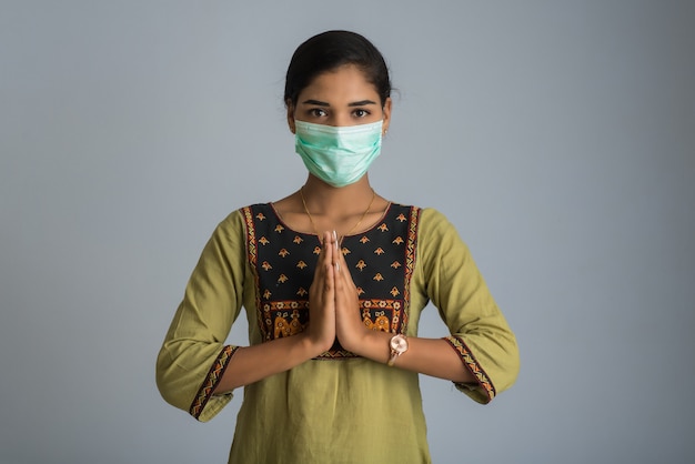 Portrait d'une jeune fille portant un masque médical faisant des voeux avec le geste Namaste.