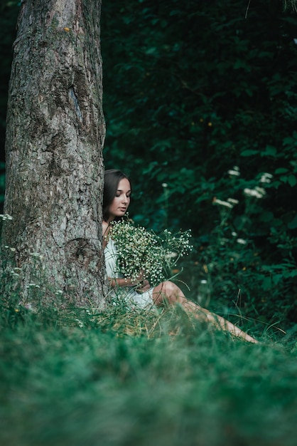 Photo portrait d'une jeune fille près d'un arbre avec des fleurs blanches dans les mains