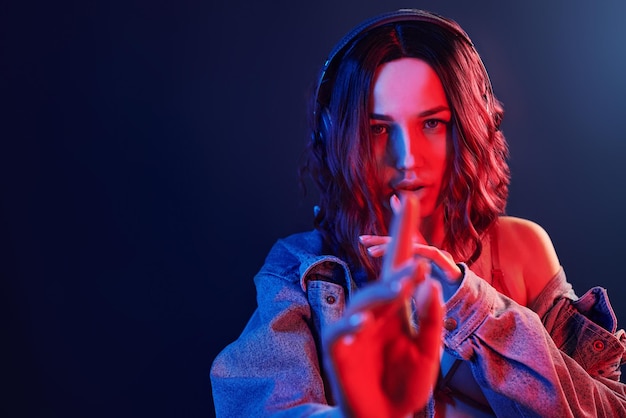 Portrait de jeune fille qui écoute de la musique dans des écouteurs en néon rouge et bleu en studio