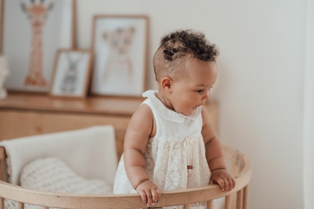 Portrait d'une jeune fille de race mixte dans un berceau en bois rond dans une chambre d'enfant confortable dans des tons neutres