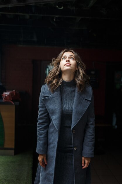 Portrait de jeune fille réfléchie en manteau gris et col roulé posant à l'extérieur