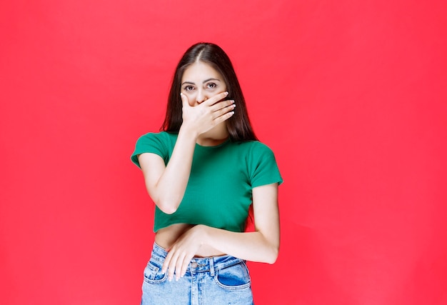 Portrait de jeune fille regardant la caméra et couvrant sa bouche sur fond rouge.