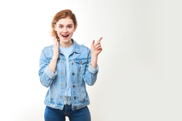 Portrait d'une jeune fille rousse sur fond blanc isolé en jeans. Regarde dans la caméra