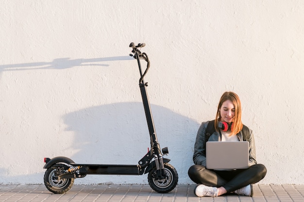 Portrait de jeune fille avec scooter électrique Woman using laptop sitting in city street