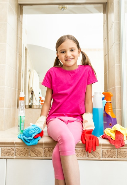 Portrait de jeune fille souriante assise sur l'évier de la salle de bain tout en faisant le nettoyage