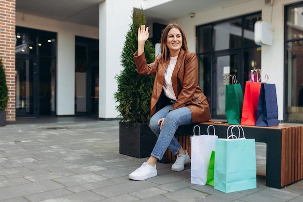 Portrait d'une jeune fille souriante assise près du centre commercial Fille tenant des sacs à provisions colorés Le concept de shopping Vente