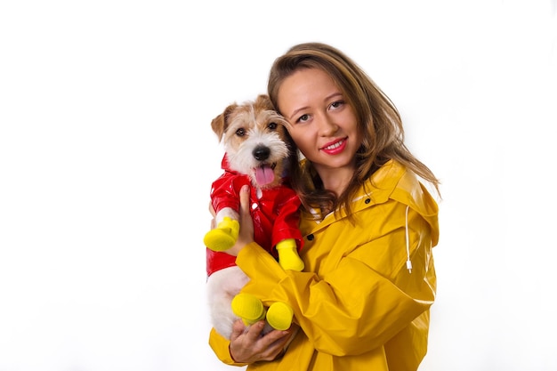 Portrait d'une jeune fille souriante dans un imperméable jaune avec un chien Jack Russell Terrier dans une veste rouge dans ses bras. Isolé sur fond blanc