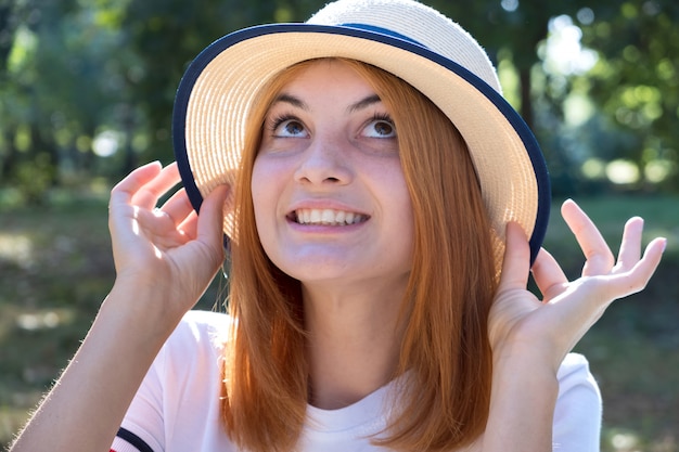 Portrait de jeune fille souriante heureuse aux cheveux rouges et au chapeau jaune à l'extérieur dans le parc de l'été.