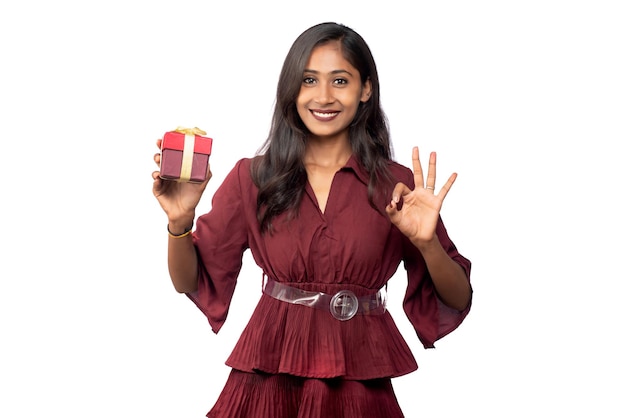 Portrait de jeune fille souriante heureuse en robe rouge tenant et posant avec boîte-cadeau sur fond blanc