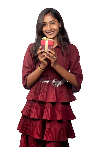 Portrait de jeune fille souriante heureuse en robe rouge tenant et posant avec boîte-cadeau sur fond blanc