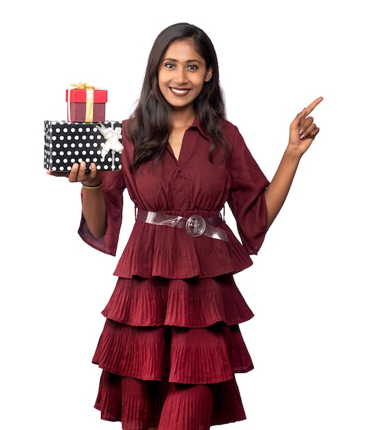 Portrait de jeune fille souriante heureuse en robe rouge tenant et posant avec boîte-cadeau sur fond blanc