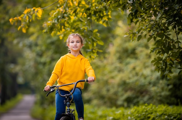 Portrait d'une jeune fille souriante en sweat-shirt jaune avec vélo dans un parc en automne