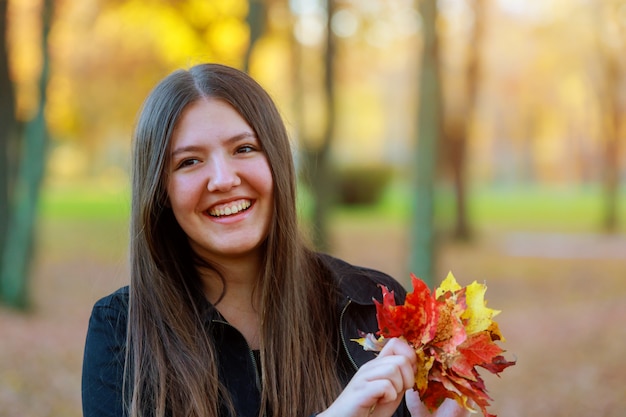 Portrait d&#39;une jeune fille souriante tenant dans la main un bouquet de feuilles d&#39;érable automne.