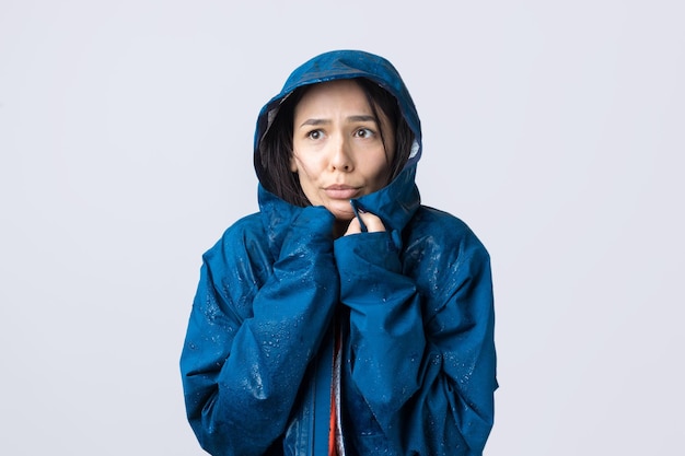 Portrait d'une jeune fille souriante vêtue d'un imperméable bleu en gouttes posant avec capuche sur fond gris dans un studio