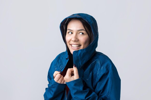 Portrait d'une jeune fille souriante vêtue d'un imperméable bleu en gouttes posant avec capuche sur gris