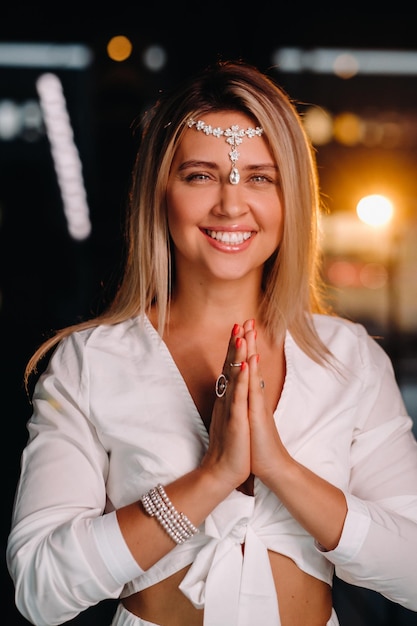 Portrait d'une jeune fille souriante vêtue d'une robe blanche, les paumes jointes devant elle