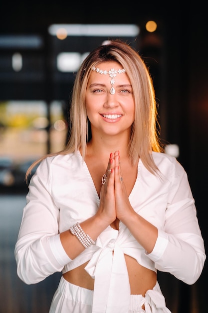 Portrait d'une jeune fille souriante vêtue d'une robe blanche, les paumes jointes devant elle