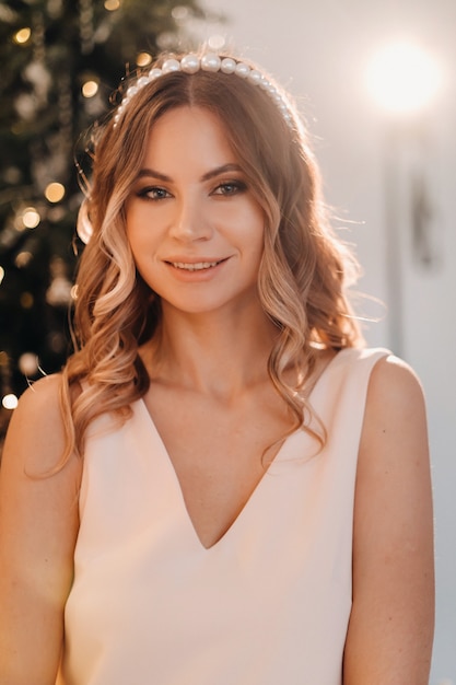 Portrait d'une jeune fille souriante vêtue d'une robe rose près de l'arbre de Noël à la maison.