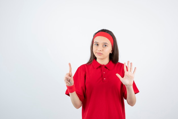 Portrait d'une jeune fille sportive debout et pointant vers le haut sur un mur blanc